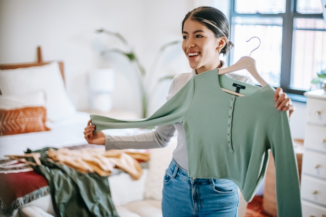 Une jeune femme range ses affaires et essaie une veste verte dans sa chambre / trier ses affaires pour la rentrée