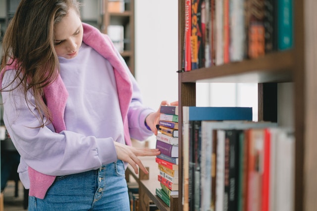 Une jeune femme cherche des livres dans une bibliothèque. / trier ses affaires pour la rentrée
