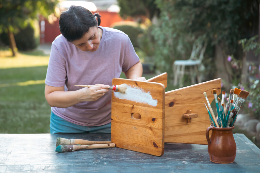 Une femme repeint un meuble en bois et relooke son meuble en bois.