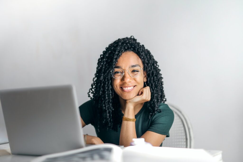 Une jeune femme à lunettes, souris devant un ordinateur, assise à un bureau / se meubler pas quand on est étudiant