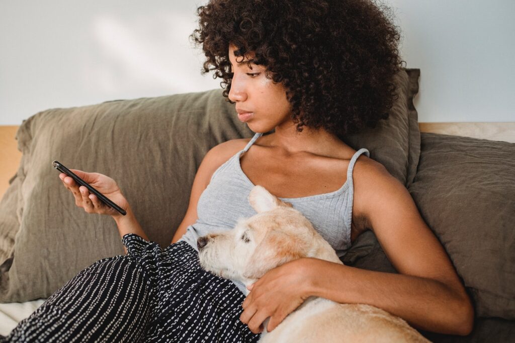 Une jeune femme utilise son smartphone assise sur son lit avec son chien / recycler ses vieux livres