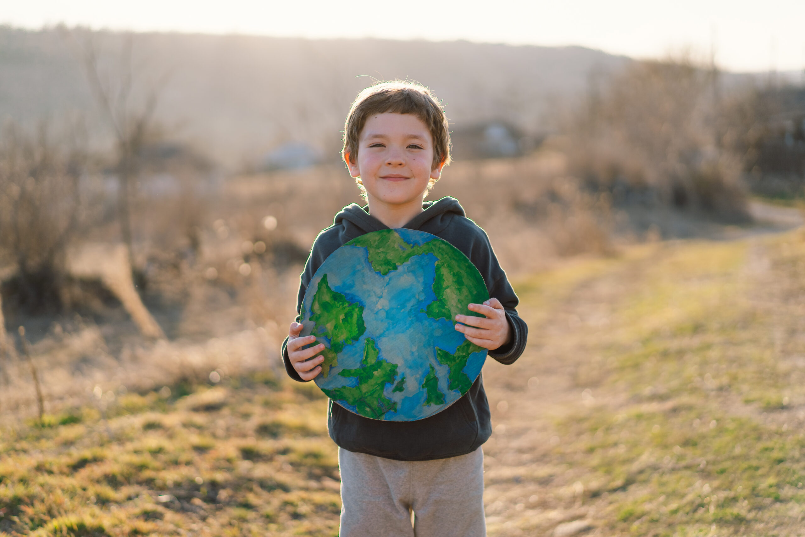 Little boy holding planet in hands against green spring background. Earth day